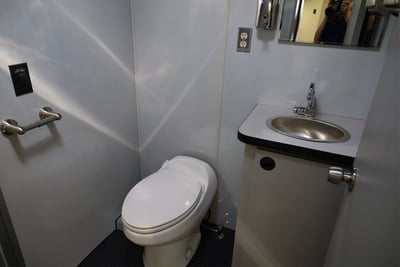 A bathroom with a toilet , sink and mirror is pictured on the inside of a rehabilitation truck. 