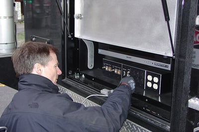 A man in a black jacket performs preventative maintenance on a mobile command truck. 