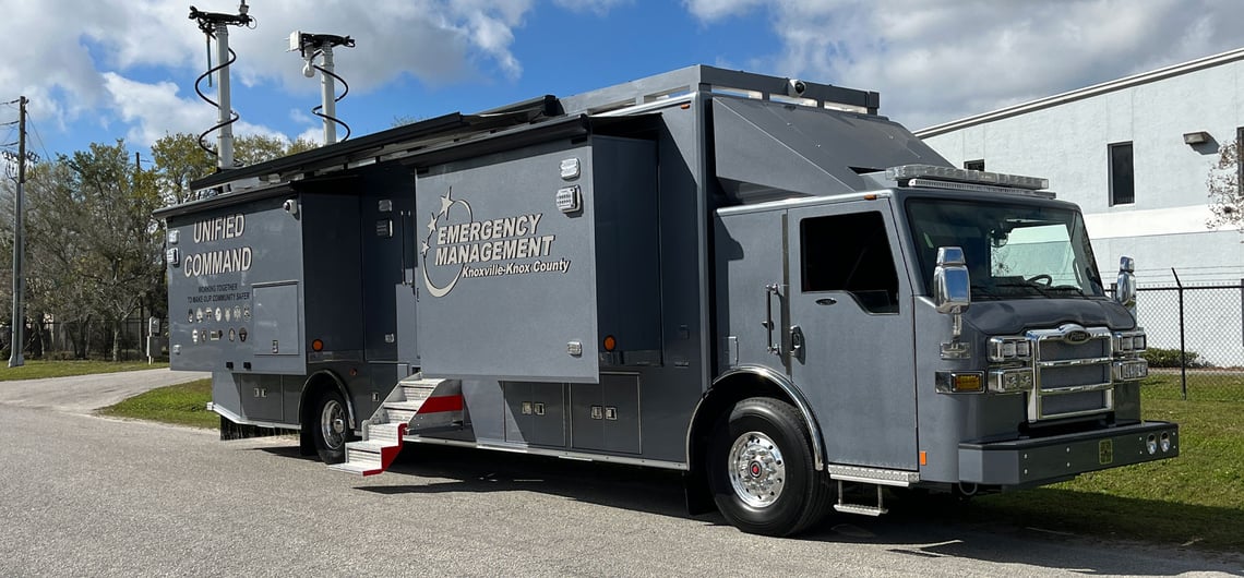 A grey mobile command vehicle is parked on an angle displaying its full SATCOM communication capabilities.  